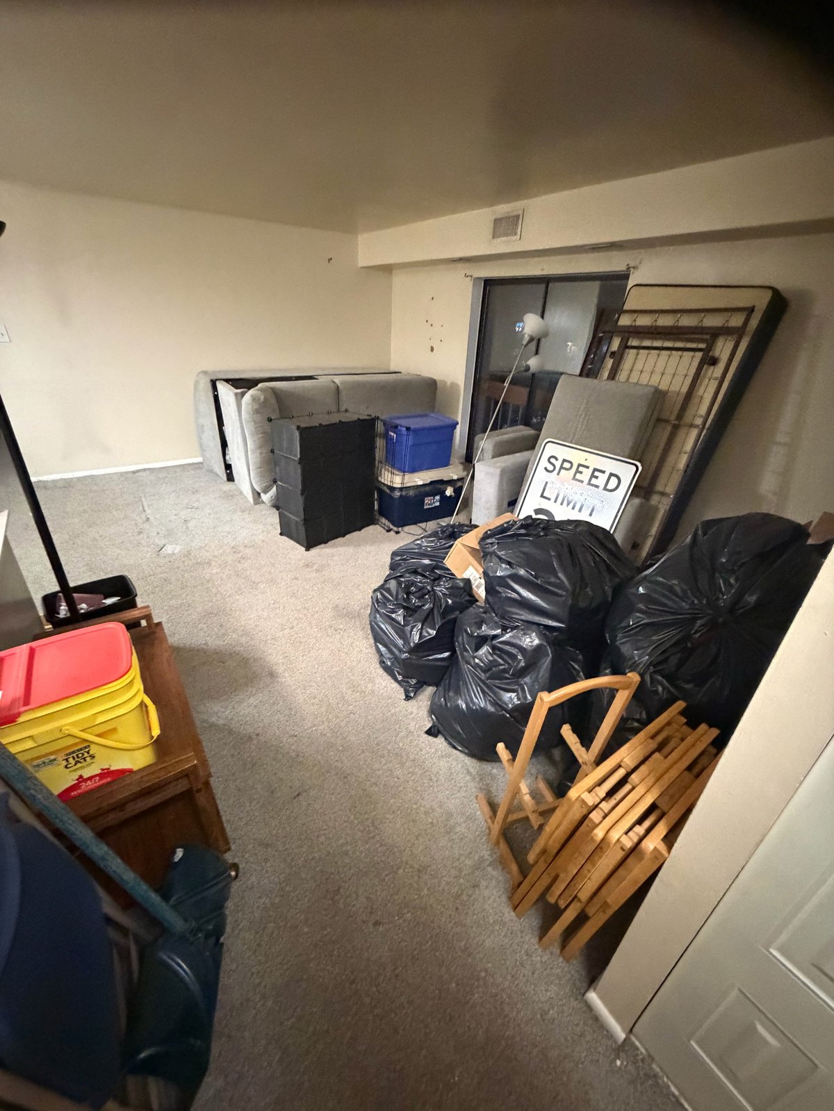 Garage basement storage room cluttered with black garbage bags, wooden chairs, and miscellaneous items scattered on concrete floor