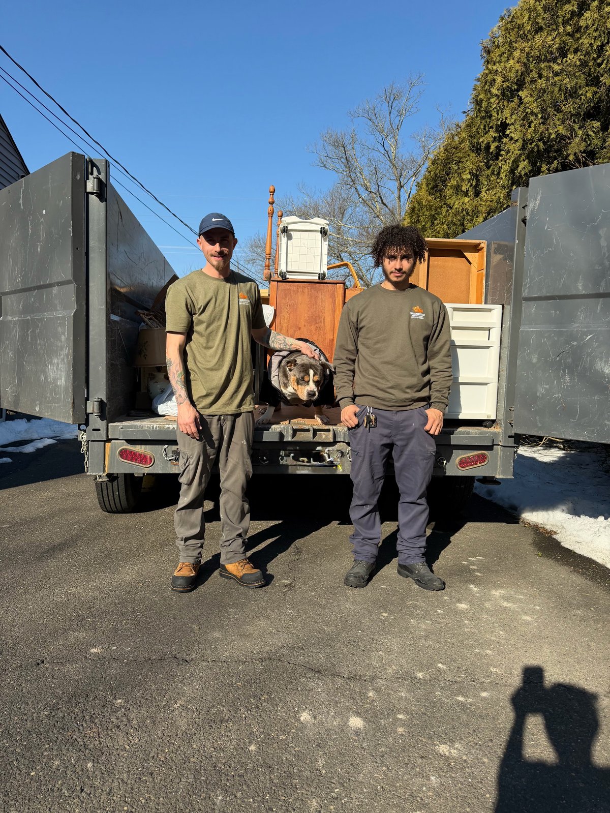 Two men posing in front of moving trucks loaded with wooden furniture boxes